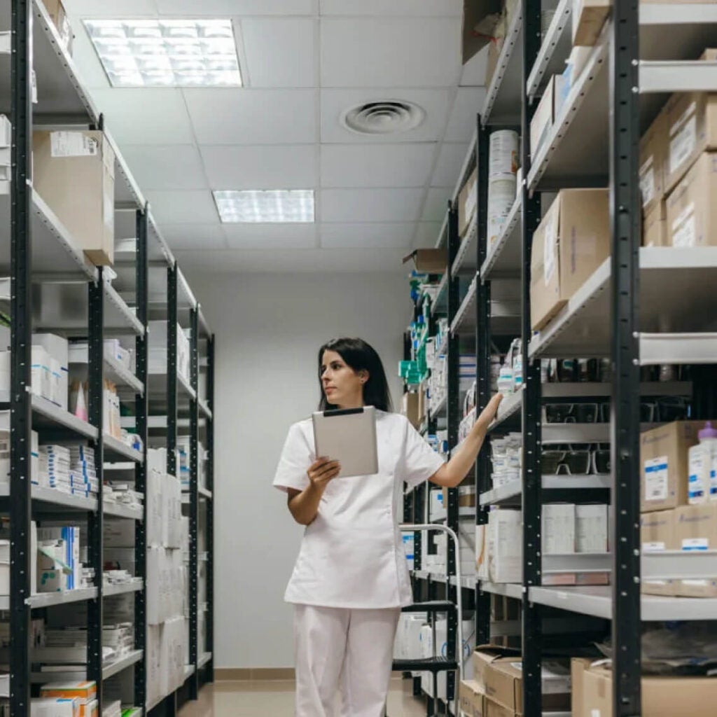 A healthcare professional uses a tablet in a storage room.